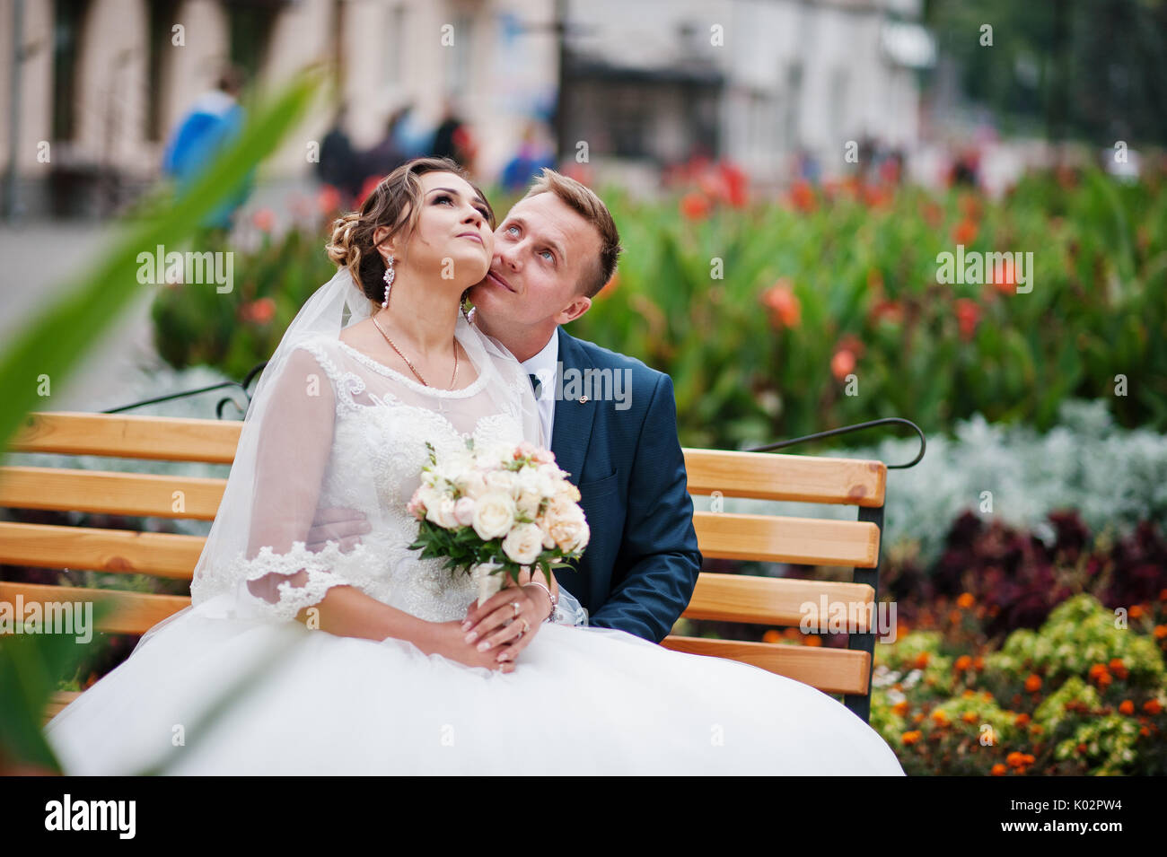Elegant wedding couple sitting on a bench in the park and looking at ...