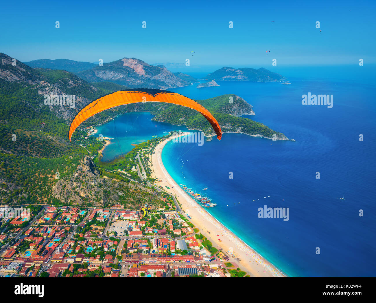 Paragliding in the sky. Paraglider tandem flying over the sea with blue water and mountains in bright sunny day. Aerial view of paraglider and Blue La Stock Photo