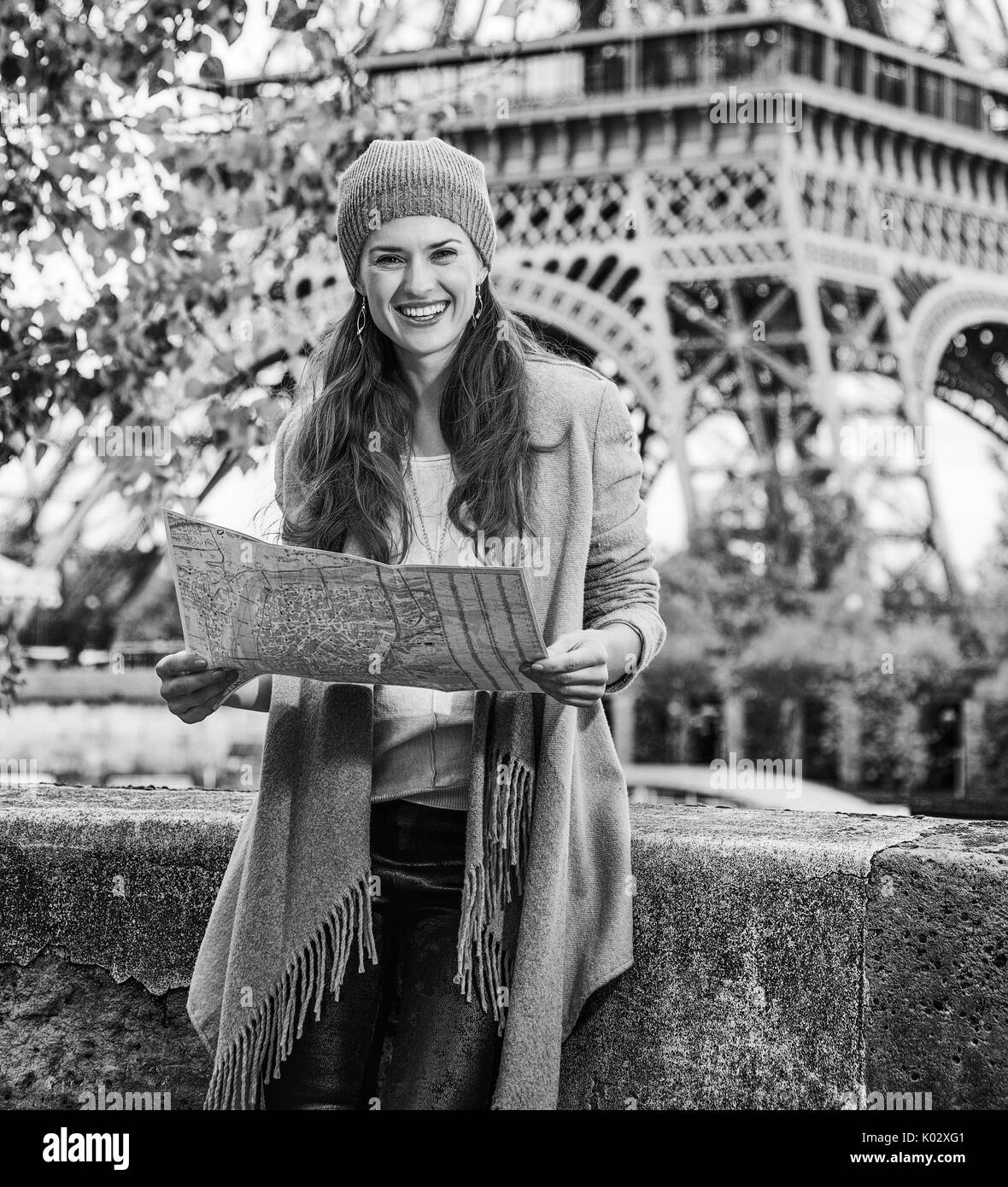 Autumn getaways in Paris. Portrait of smiling young tourist woman on embankment near Eiffel tower in Paris, France with map Stock Photo