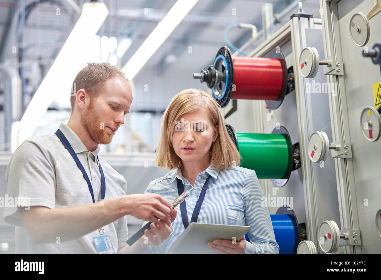 Male and female workers with digital tablet examining part in fiber optics factory Stock Photo