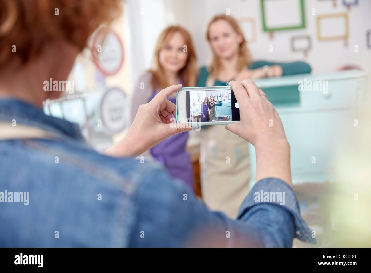 Woman with camera phone photographing classmates posing at painted side table in art class workshop Stock Photo