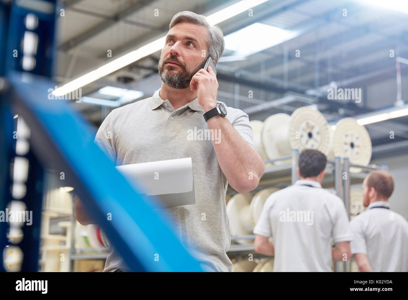 Male supervisor with clipboard talking on cell phone in fiber optics factory Stock Photo