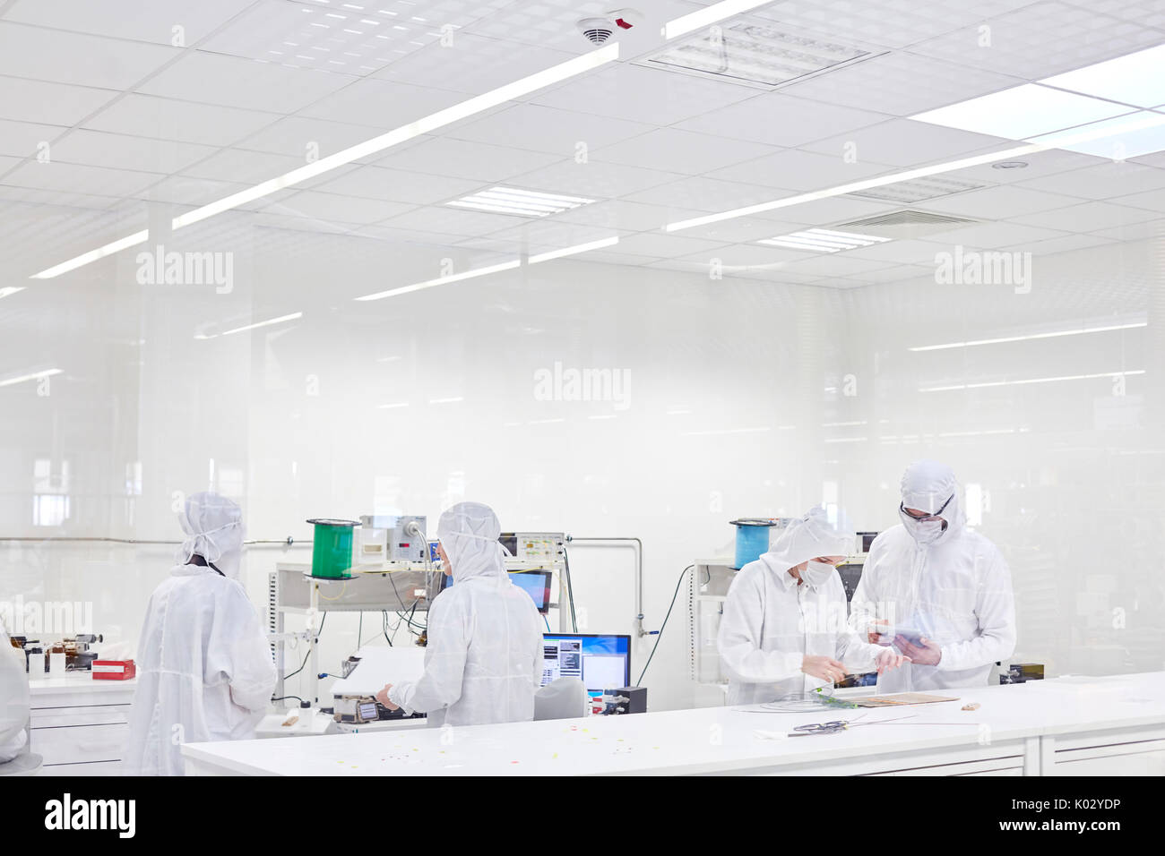 Engineers in clean suits using machinery in fiber optics research and testing lab Stock Photo