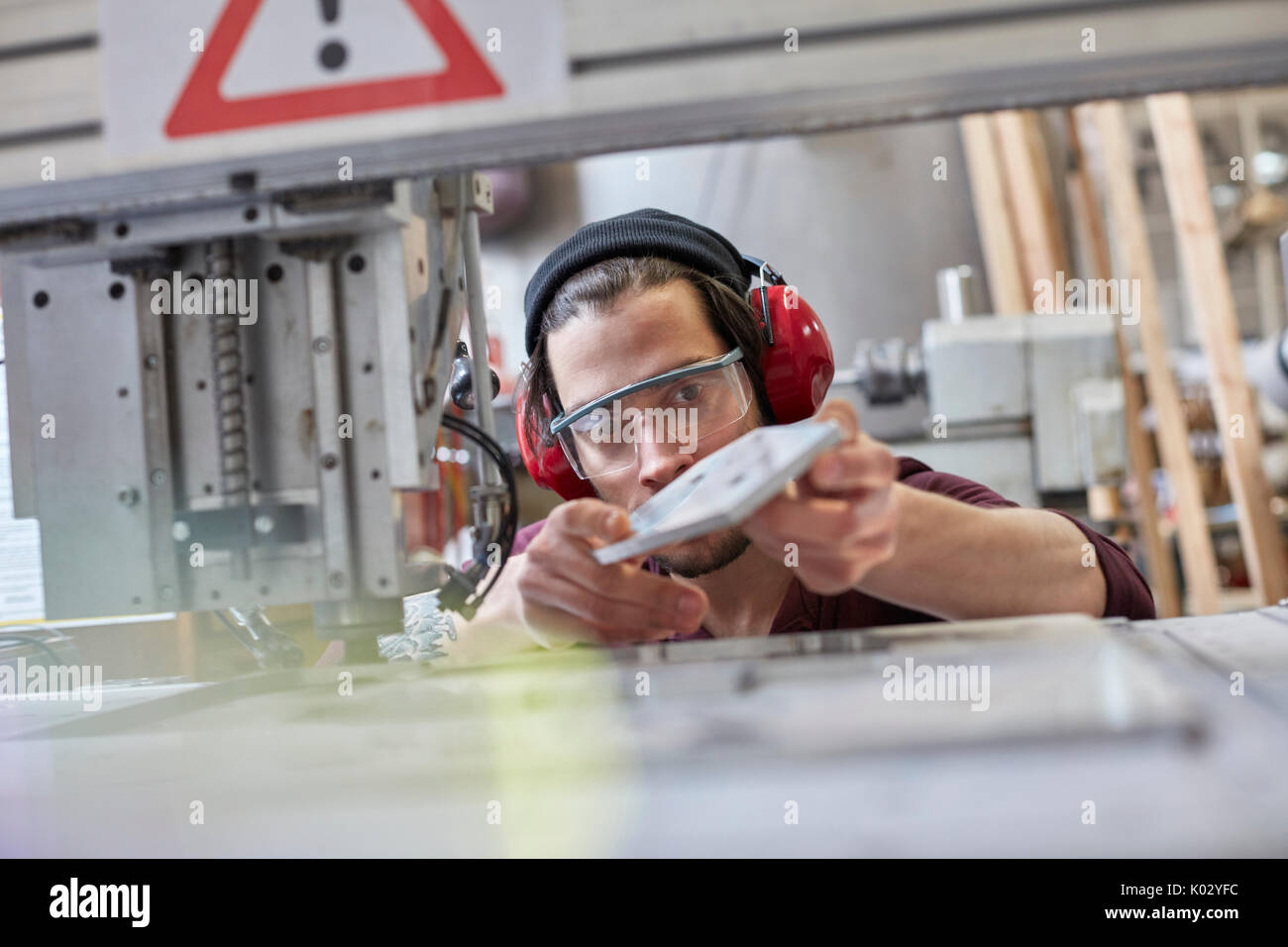 Male designer wearing ear protectors, examining prototype in workshop Stock Photo
