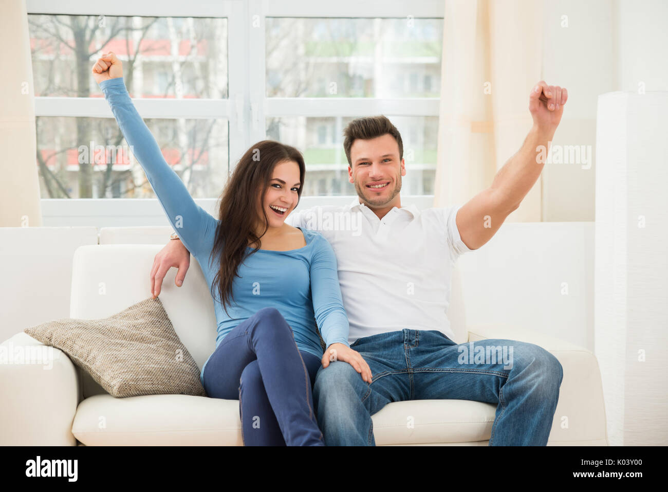 Portrait Of Ecstatic Couple Sitting On Couch At Home Stock Photo