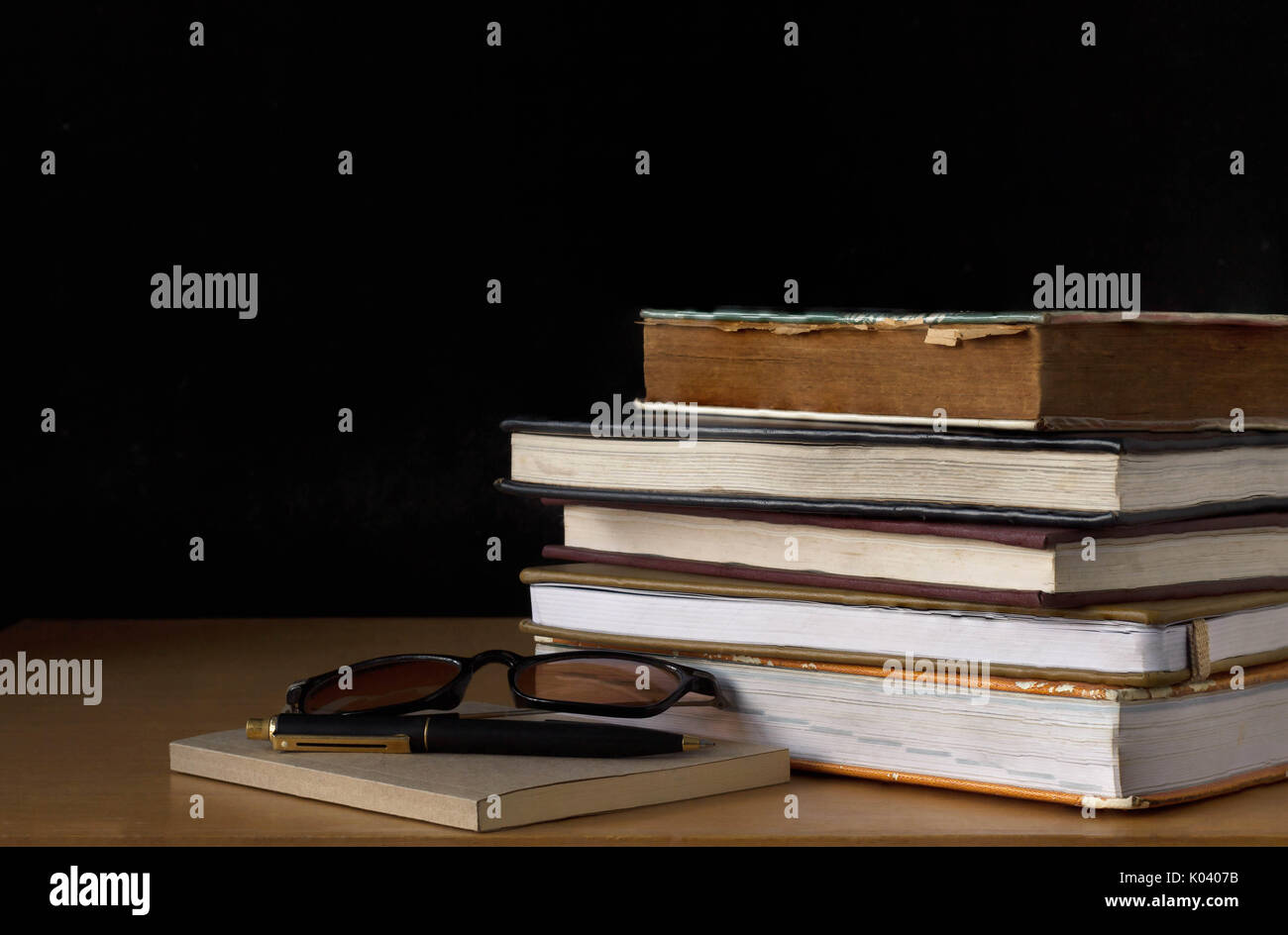 Old book stack on wooden table with black background Stock Photo - Alamy