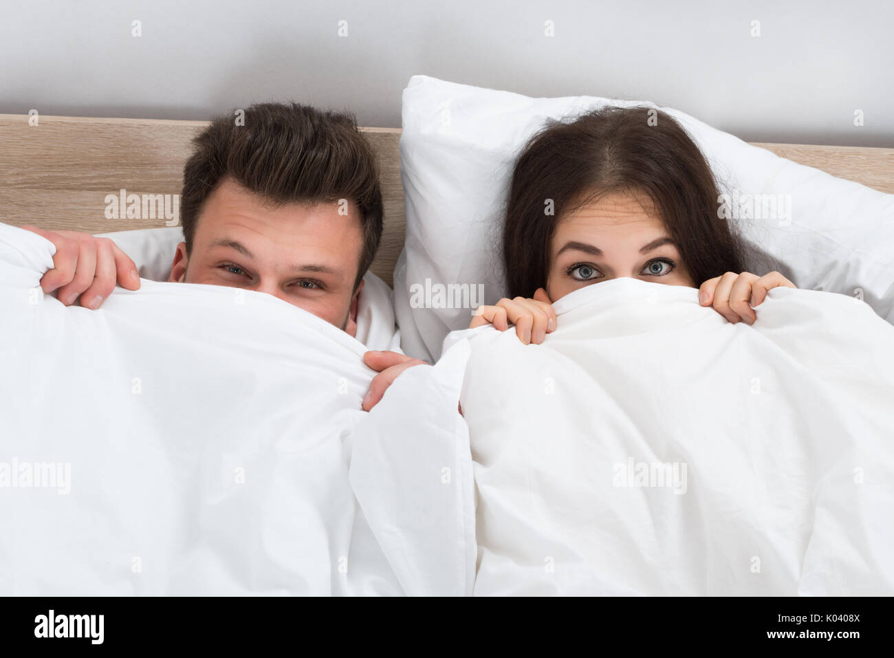 Portrait Of Young Couple Hiding Face With Blanket In Bedroom Stock Photo