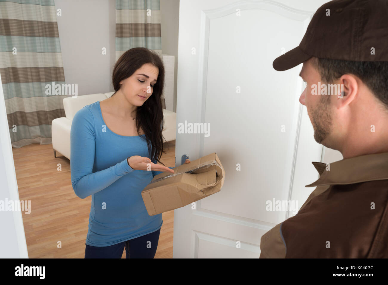 Woman Shouting On Delivery Man For Damaged Package At Doorway Stock Photo