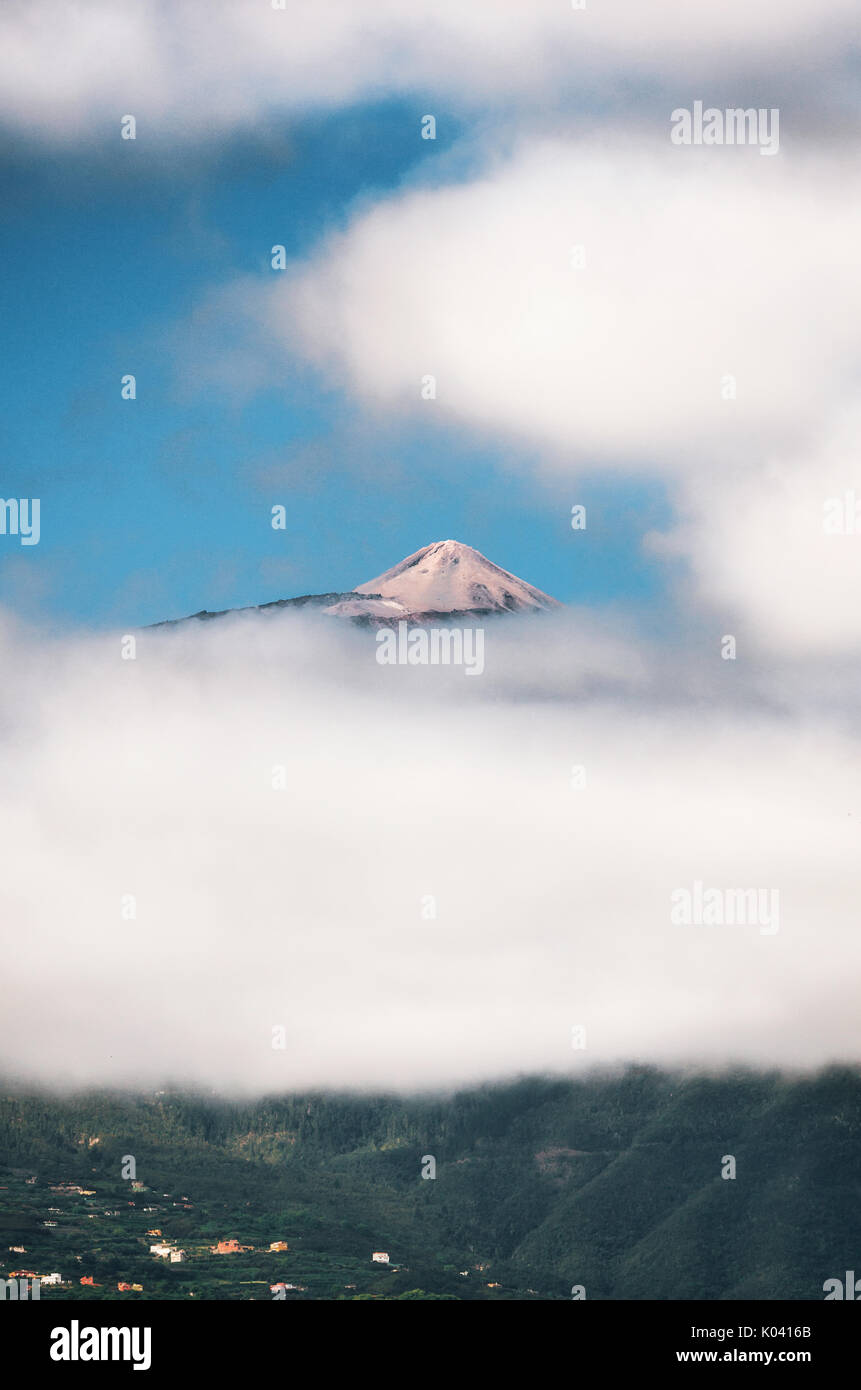 Peak of Teide, Top of Teide in clouds with the village and greenery hills in bottom. View from Puerto de la Cruz, Tenerife, Canary islands, Spain Stock Photo