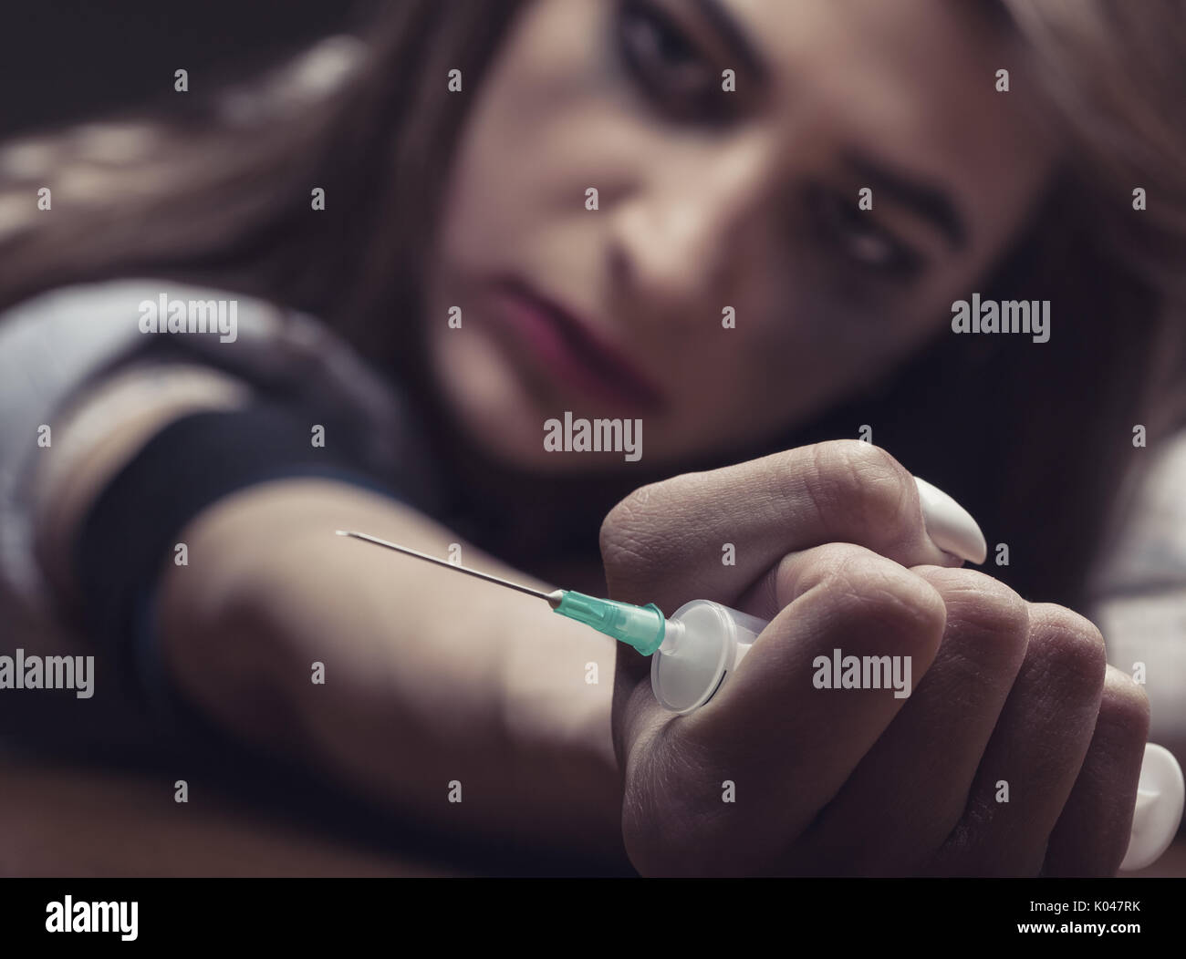 A young woman with a drug holding a syringe on dark background. Focus on hands Stock Photo