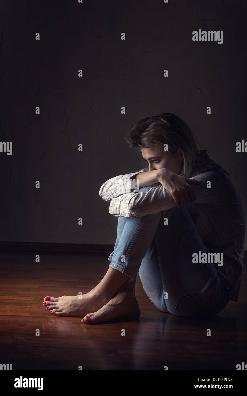 Young sad woman sitting alone on the floor in an empty room Stock Photo