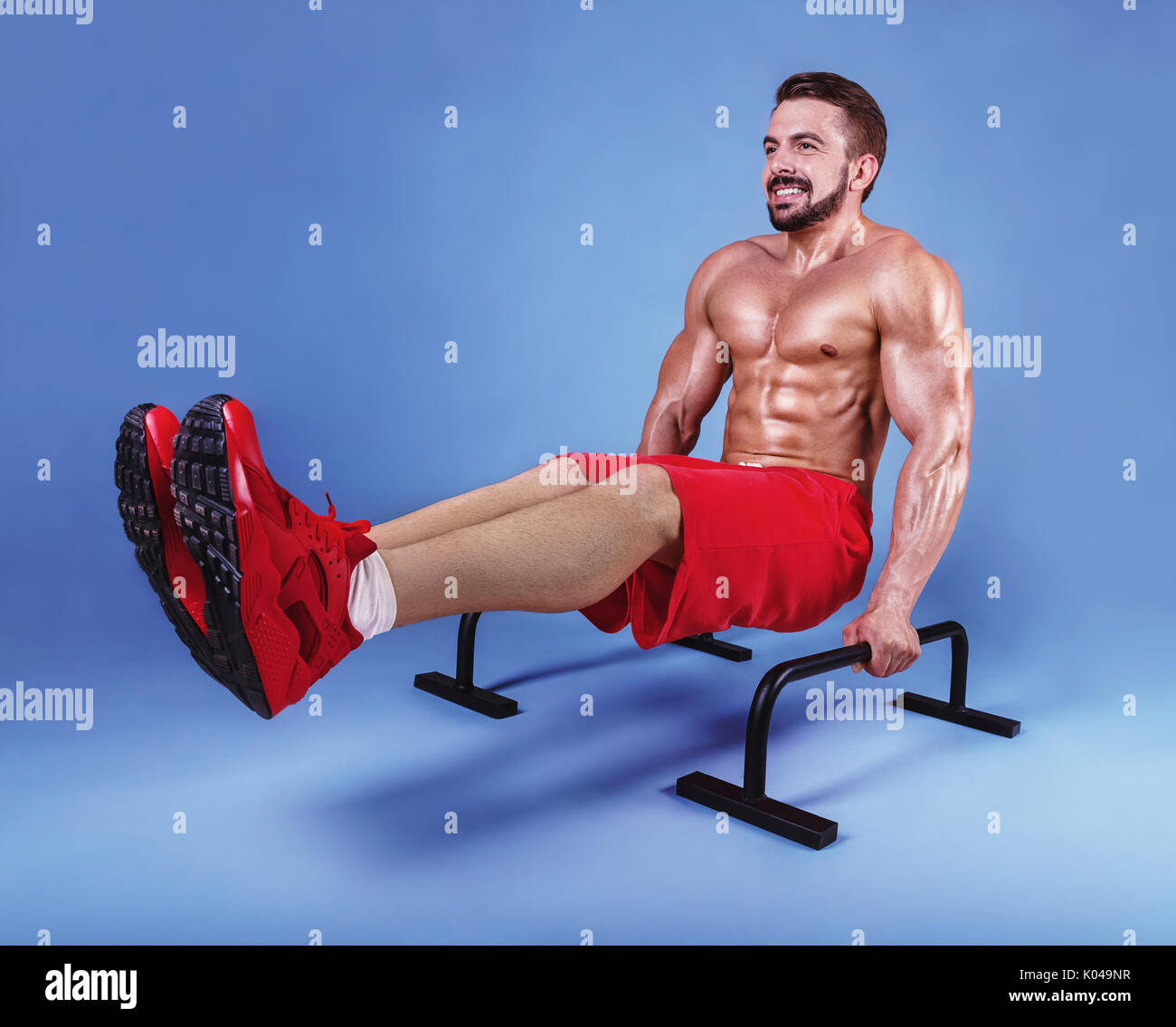 Handsome athlete working out exercise on parallel bars on a blue background. Studio shot Stock Photo