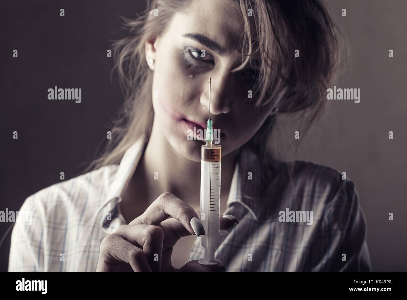 Young woman with drug addiction on dark background. Focus on syringe Stock Photo