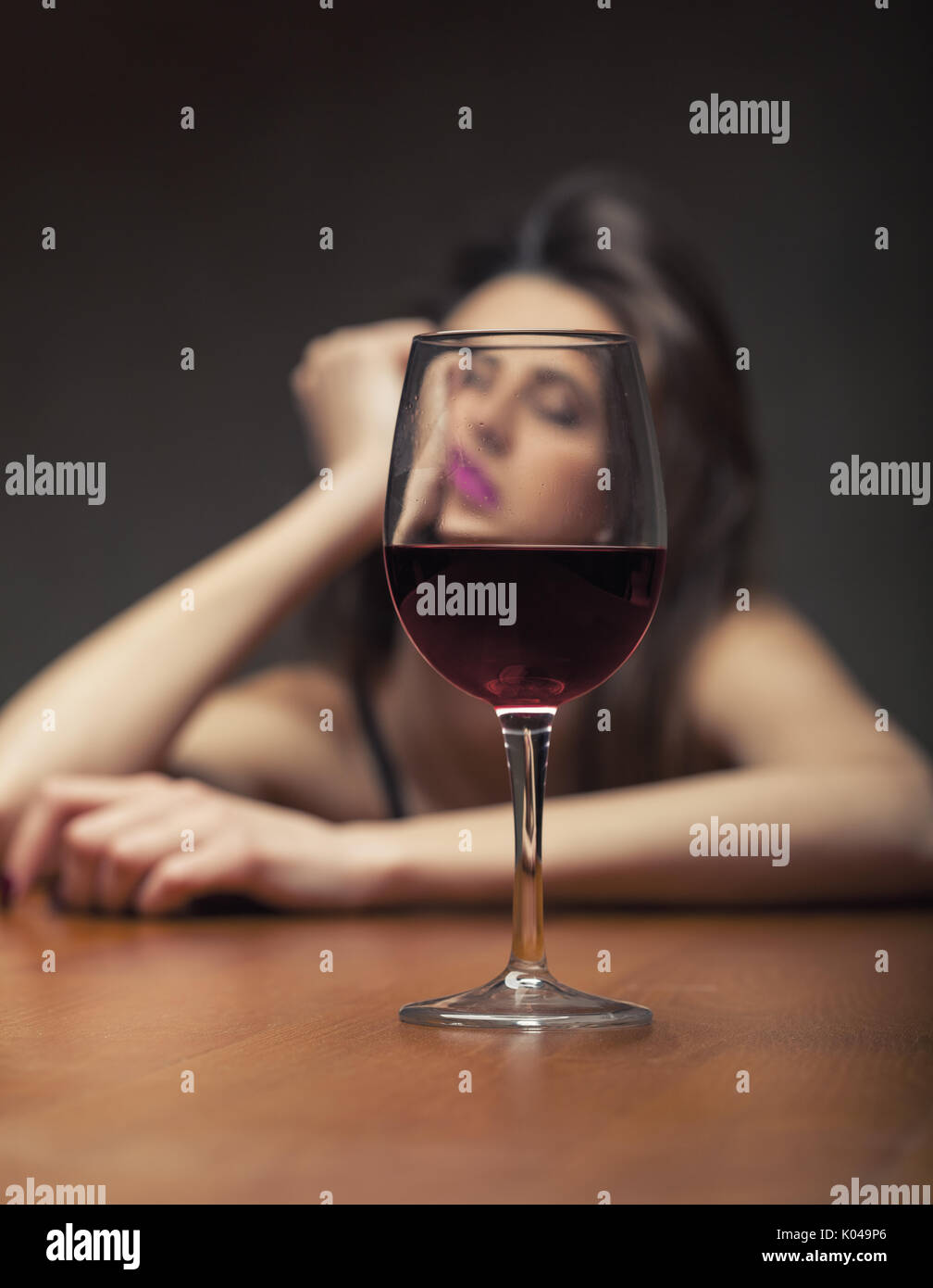 Woman in depression, drinking alcohol on dark background. Focus on the glass Stock Photo
