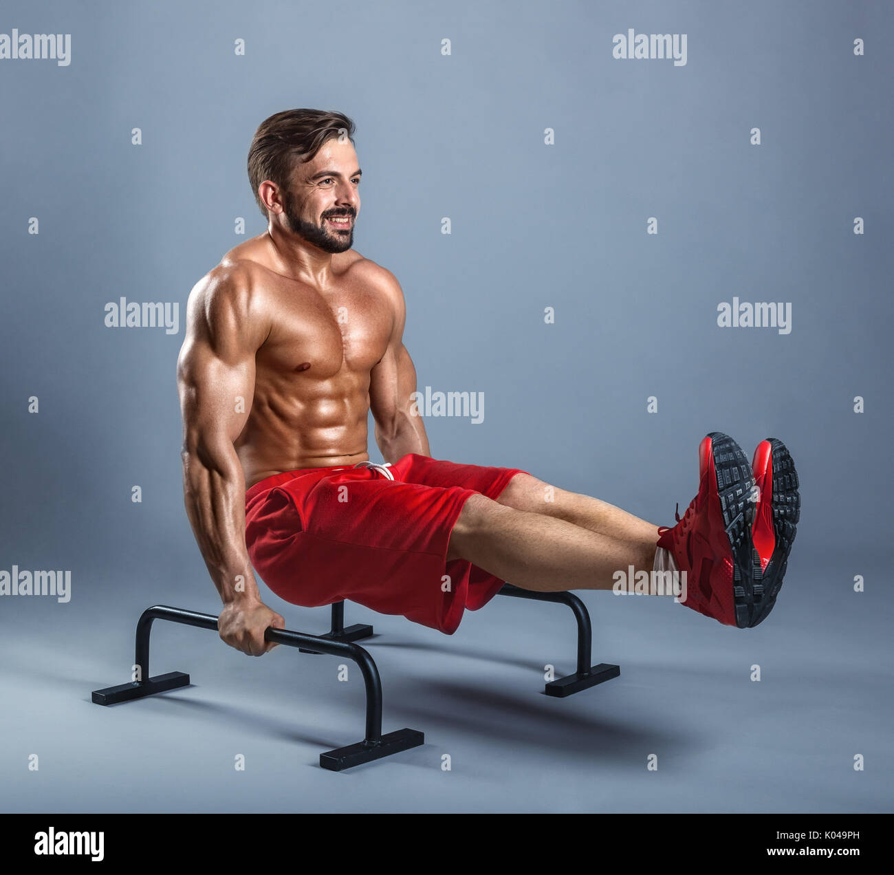 Handsome athlete working out exercise on parallel bars on a gray background Stock Photo