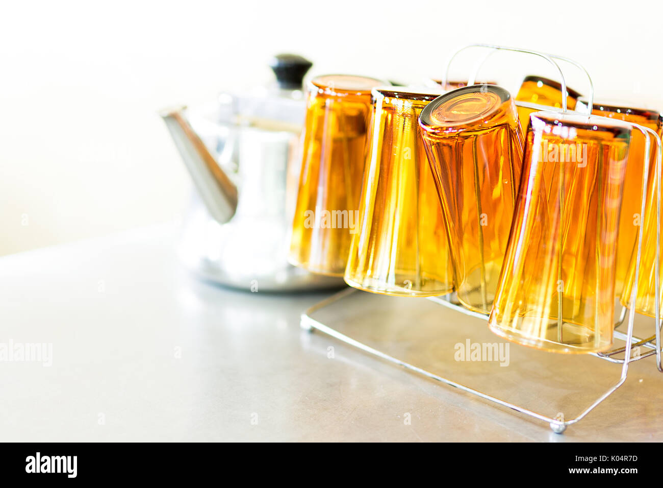 Brown chai / tea glasses on a holder next to a metal tea pot on a stainless steal table top in a restaurant. Stock Photo