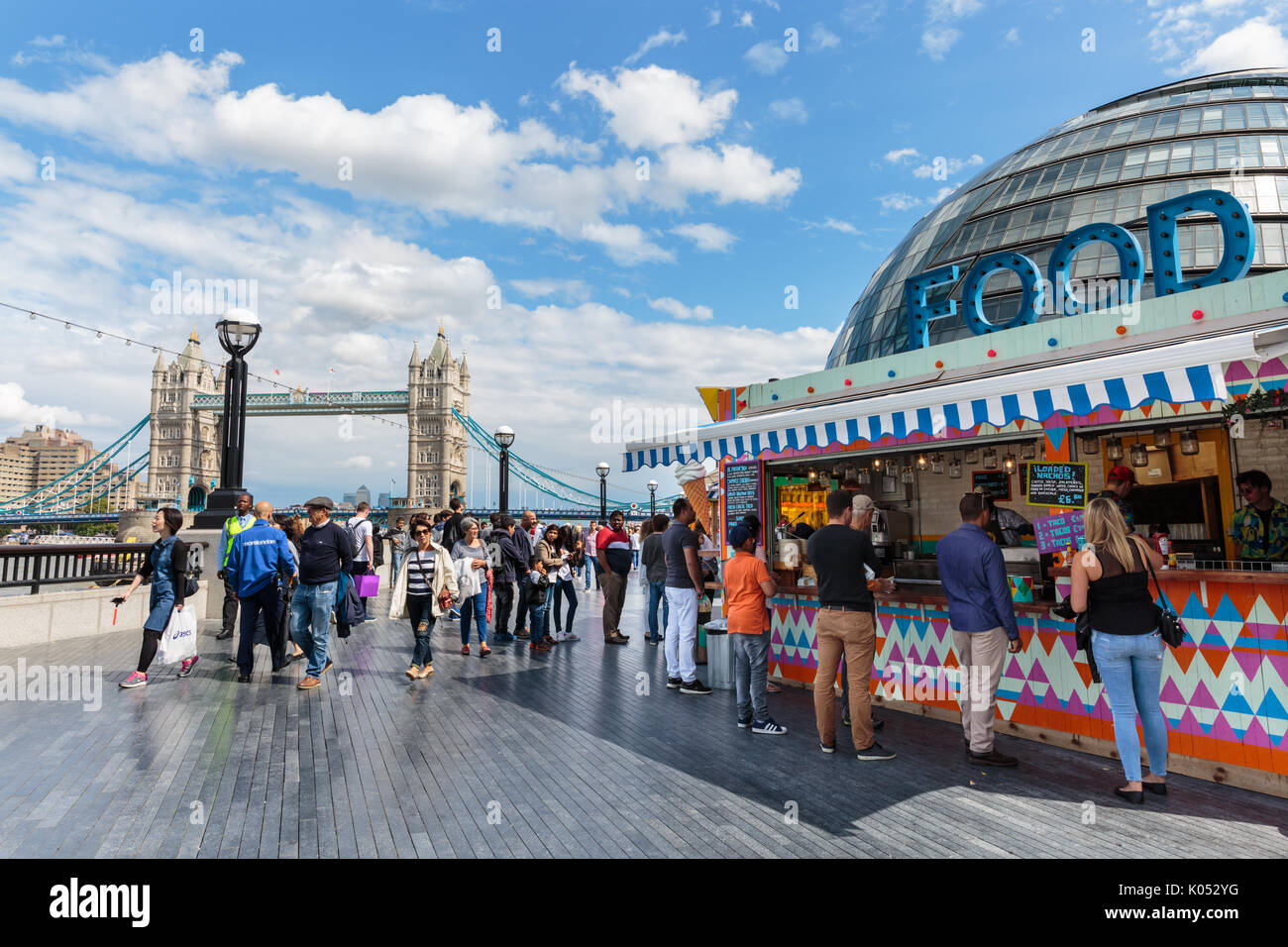 People enjoy food from a outdoor pop up stalls at More London in the summer sun with Tower Bridge and City Hall in the background, London, England Stock Photo