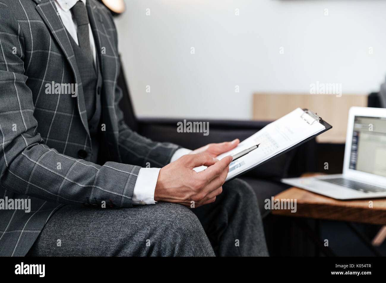 Cropped image of a man in suit analyzing documents while sitting on a couch Stock Photo