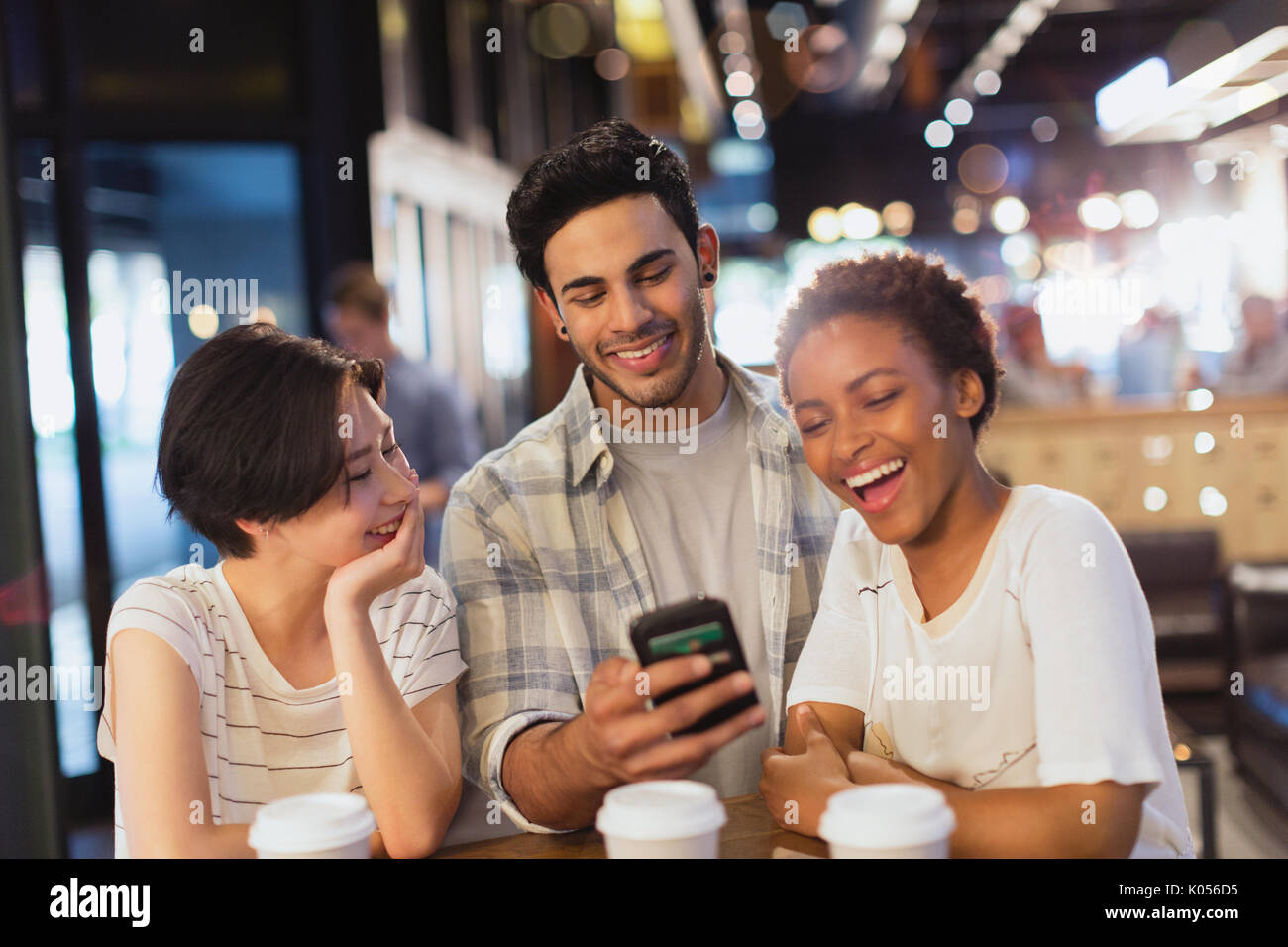 Young friends using cell phone, texting and laughing at cafe Stock Photo