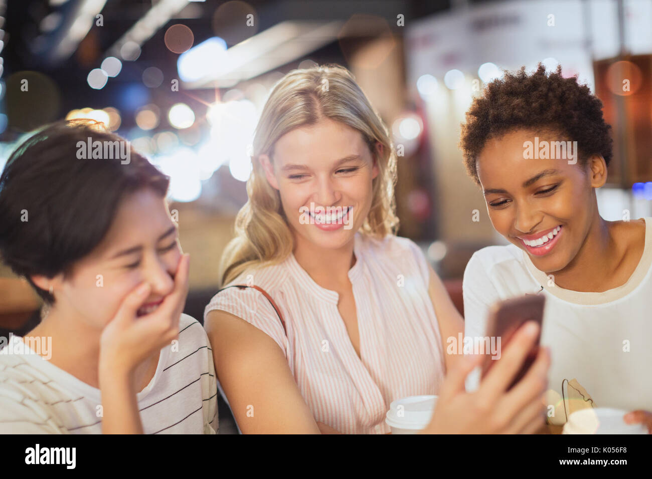 Laughing young friends with cell phone at cafe Stock Photo