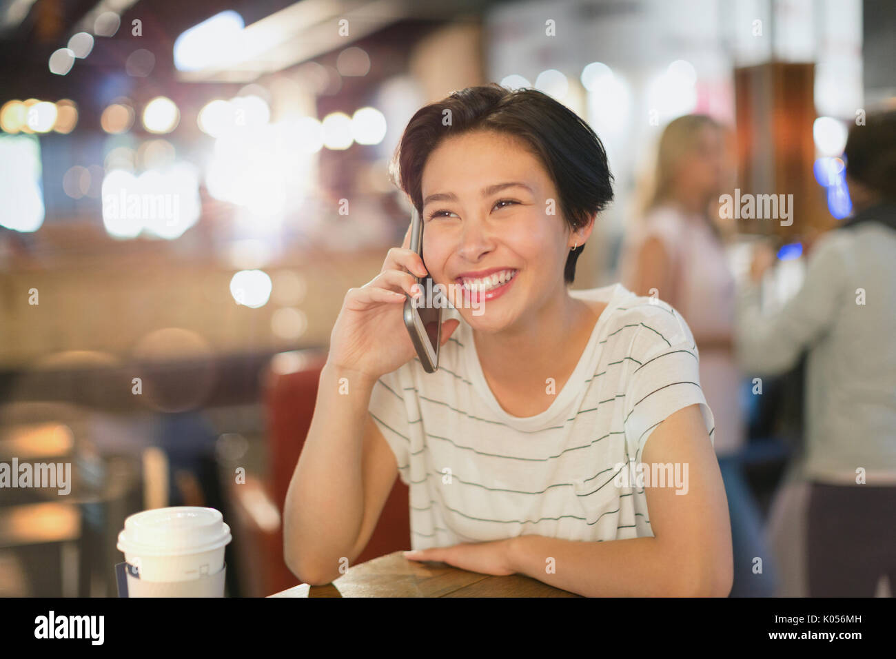 Smiling young woman talking on cell phone in cafe Stock Photo