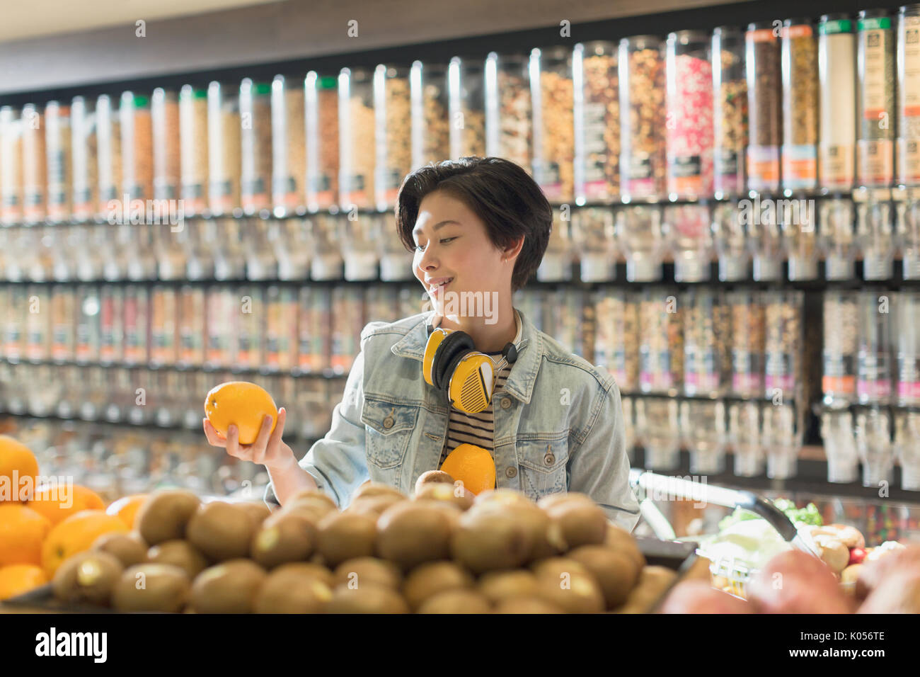 Young woman with headphones grocery shopping, holding orange in market Stock Photo