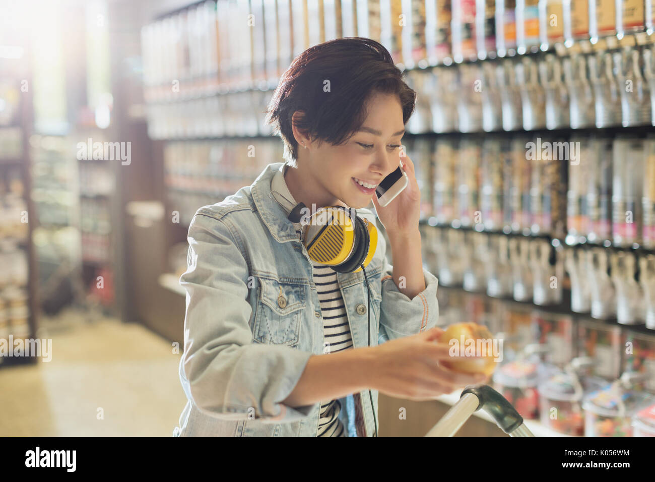 Smiling young woman with headphones talking on cell phone grocery shopping in market Stock Photo