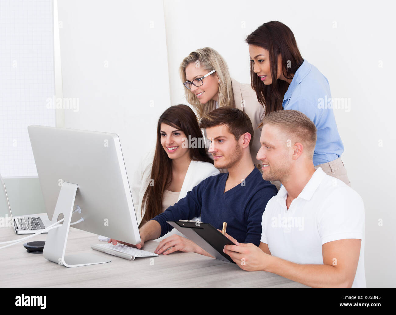 Group of smiling businesspeople using computer together in office Stock ...
