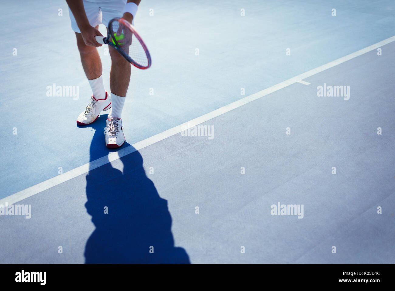 Young male tennis player preparing to serve the ball on sunny blue tennis court Stock Photo