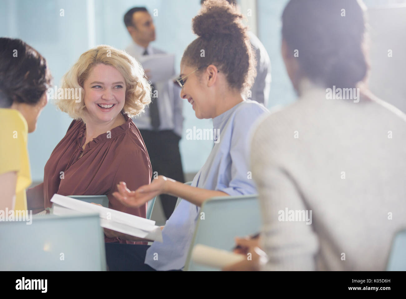 Smiling businesswomen discussing paperwork in conference audience Stock Photo