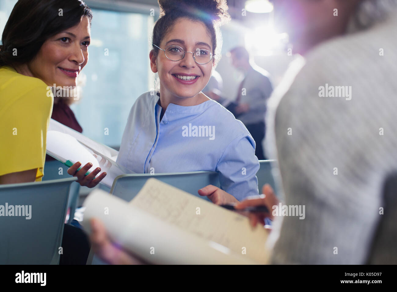 Smiling businesswomen discussing paperwork in conference audience Stock Photo