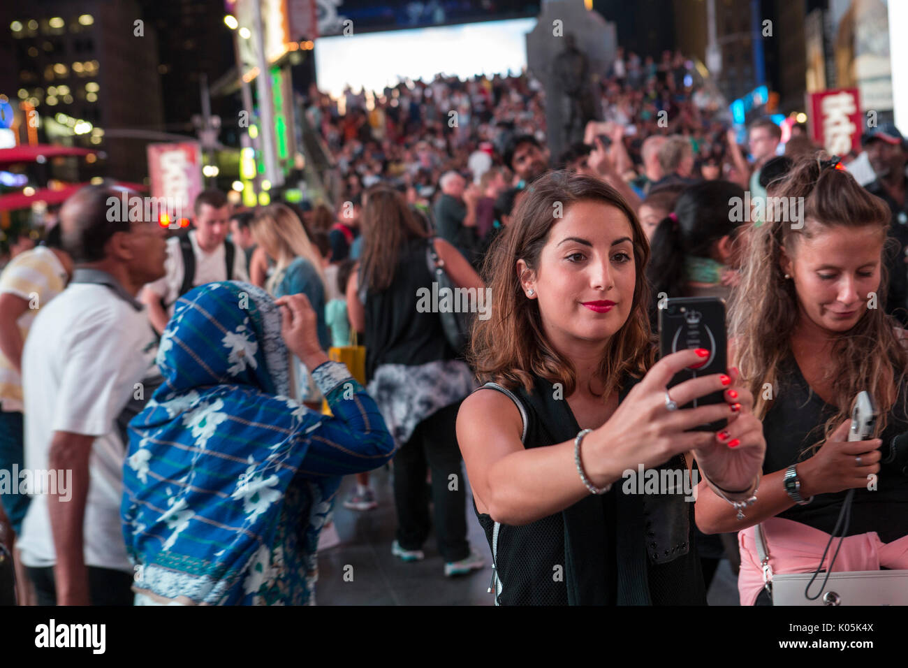 Crowds of tourists take selfies and photos at night in Times Square ...