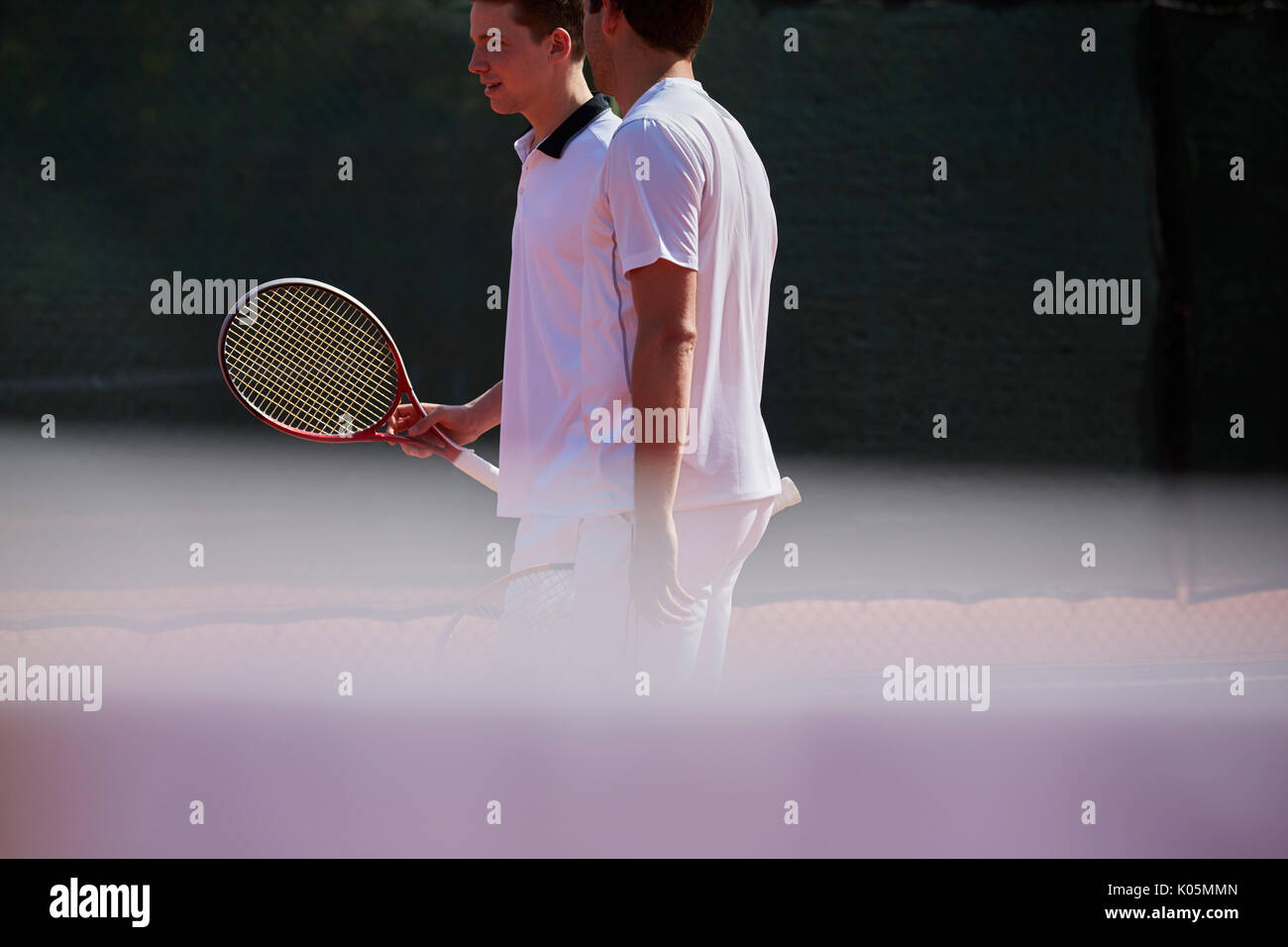 Male tennis doubles talking on sunny tennis court Stock Photo