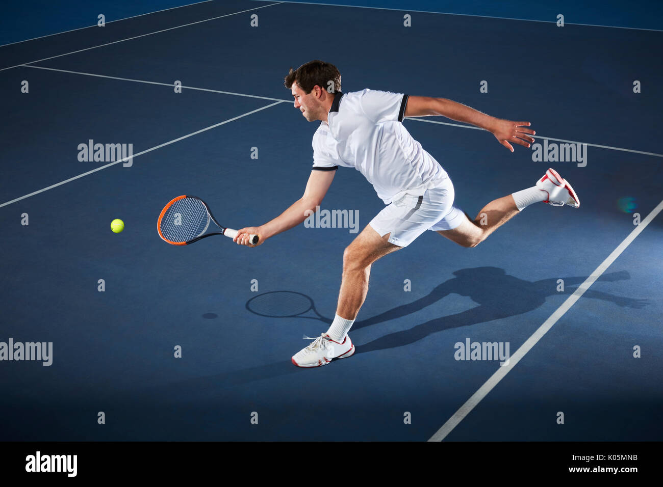 Male tennis player playing tennis, reaching with tennis racket on tennis court Stock Photo