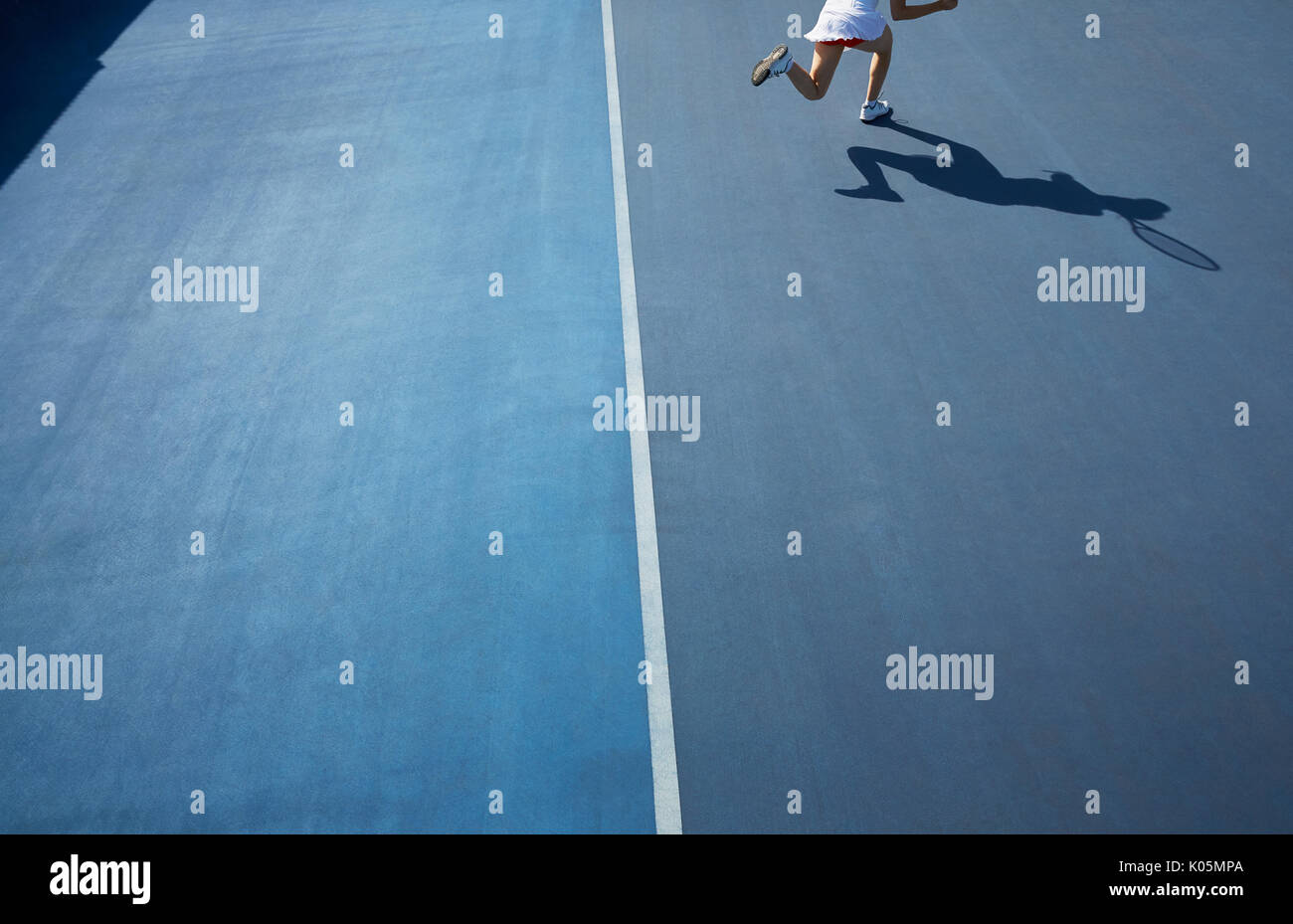 Shadow of female tennis player running on sunny blue tennis court Stock Photo