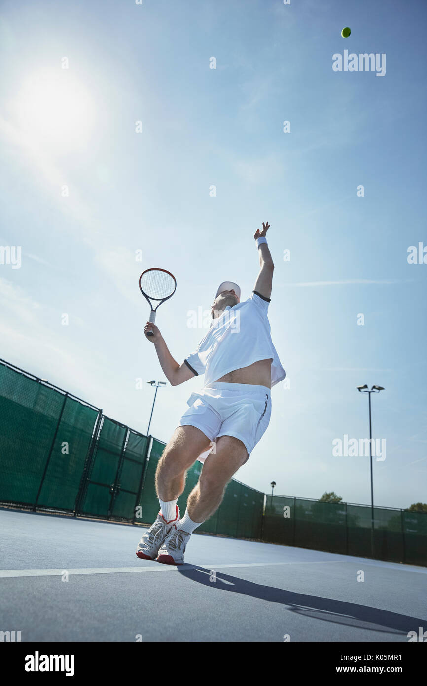 Young male tennis player playing tennis, serving the ball on sunny tennis court Stock Photo