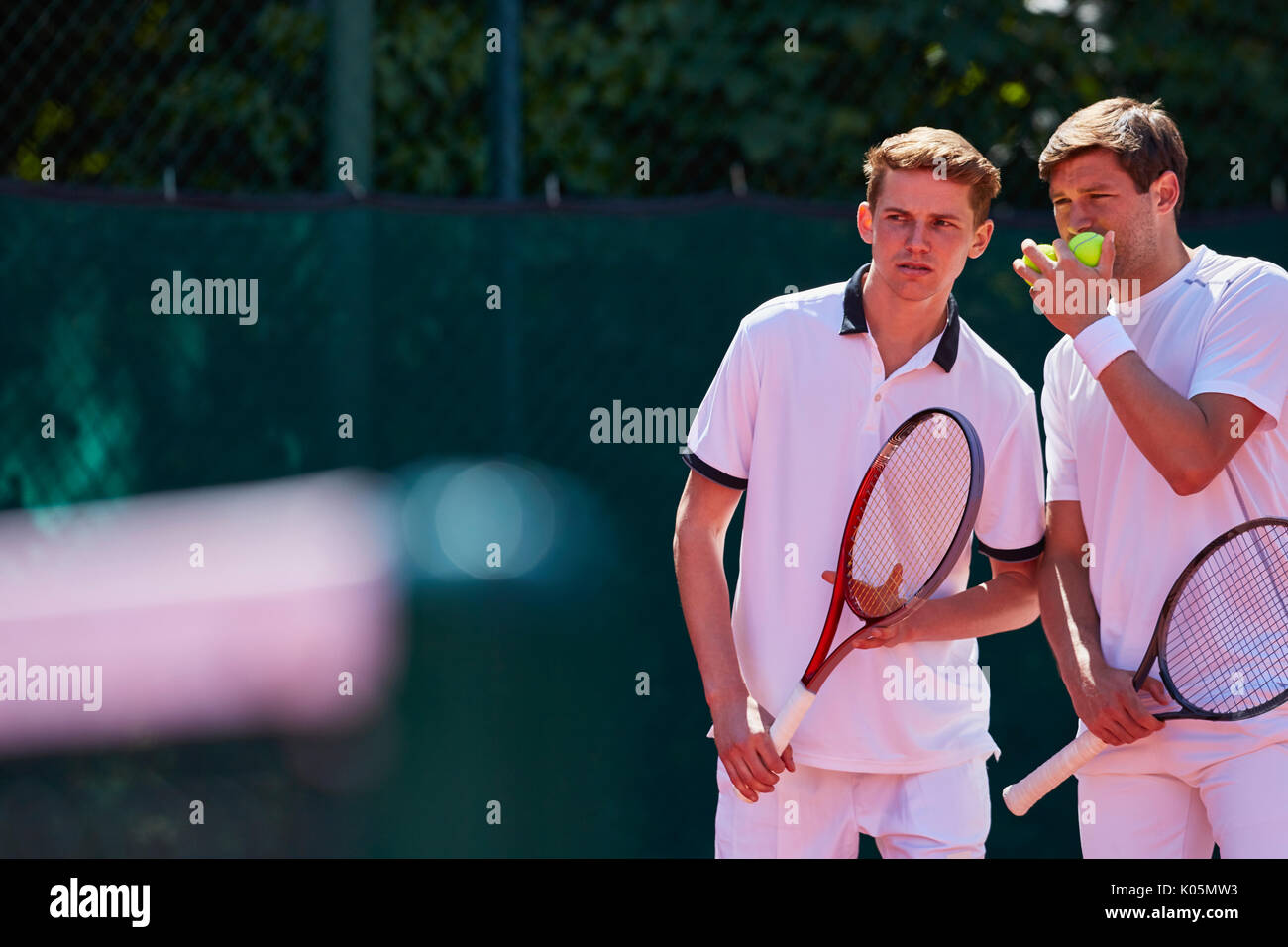 Young male tennis doubles players talking, strategizing Stock Photo