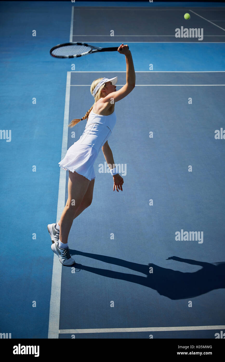 Young female tennis player playing tennis, reaching with tennis racket on sunny blue tennis court Stock Photo