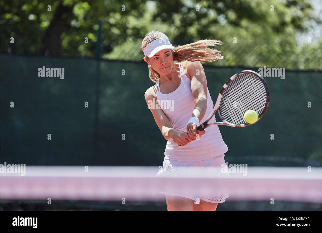 Determined young female tennis player playing tennis, hitting the ball on sunny tennis court Stock Photo