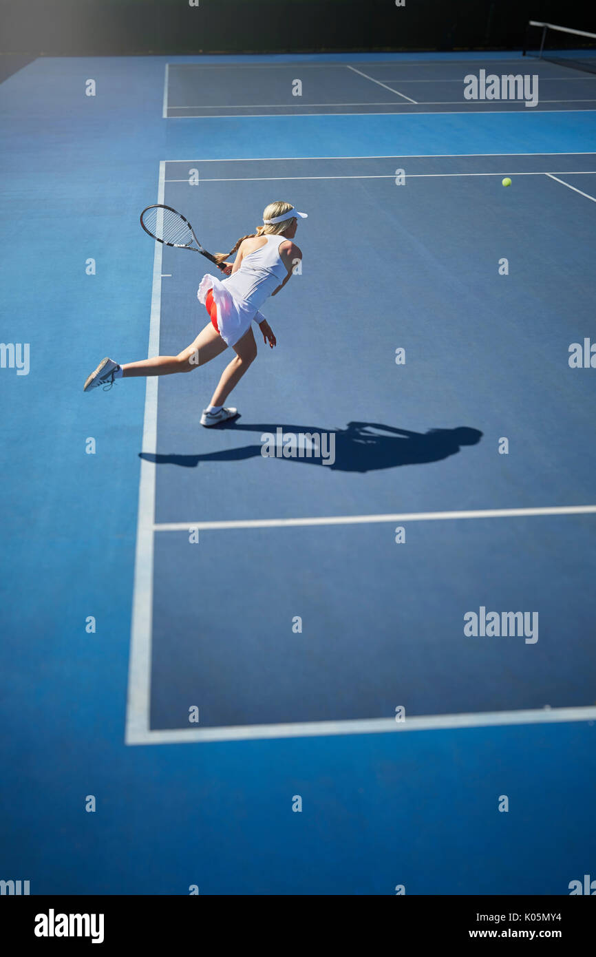 Young female tennis player playing tennis, swinging tennis racket on sunny blue tennis court Stock Photo