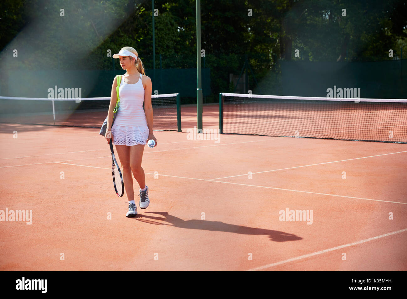 Young female tennis player walking with tennis racket on sunny clay court Stock Photo