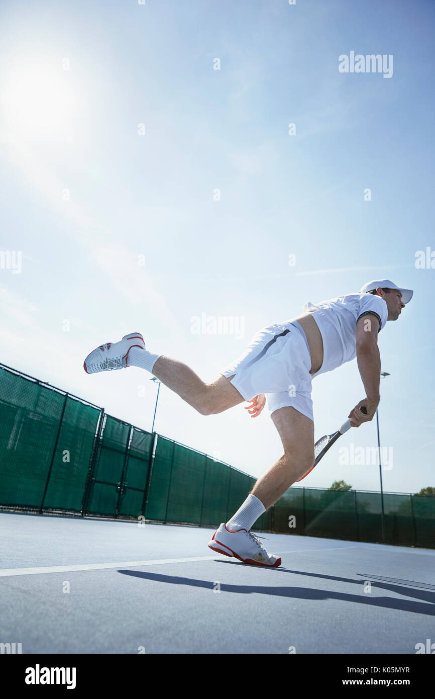 Young male tennis player playing tennis, swinging racket on sunny tennis court Stock Photo