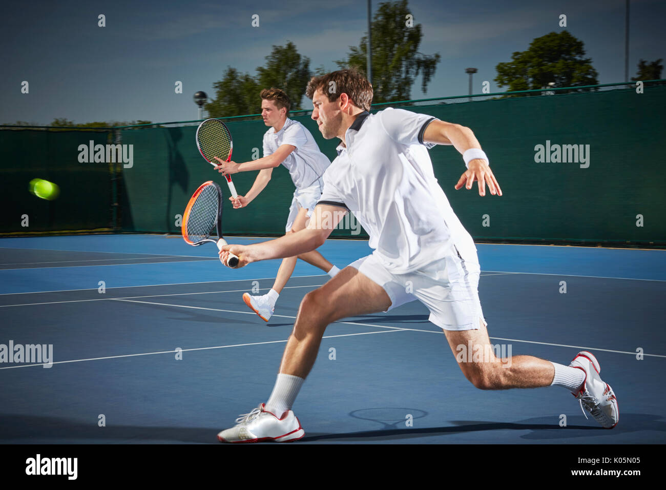 Young male tennis doubles players playing tennis, hitting the ball on blue tennis court Stock Photo