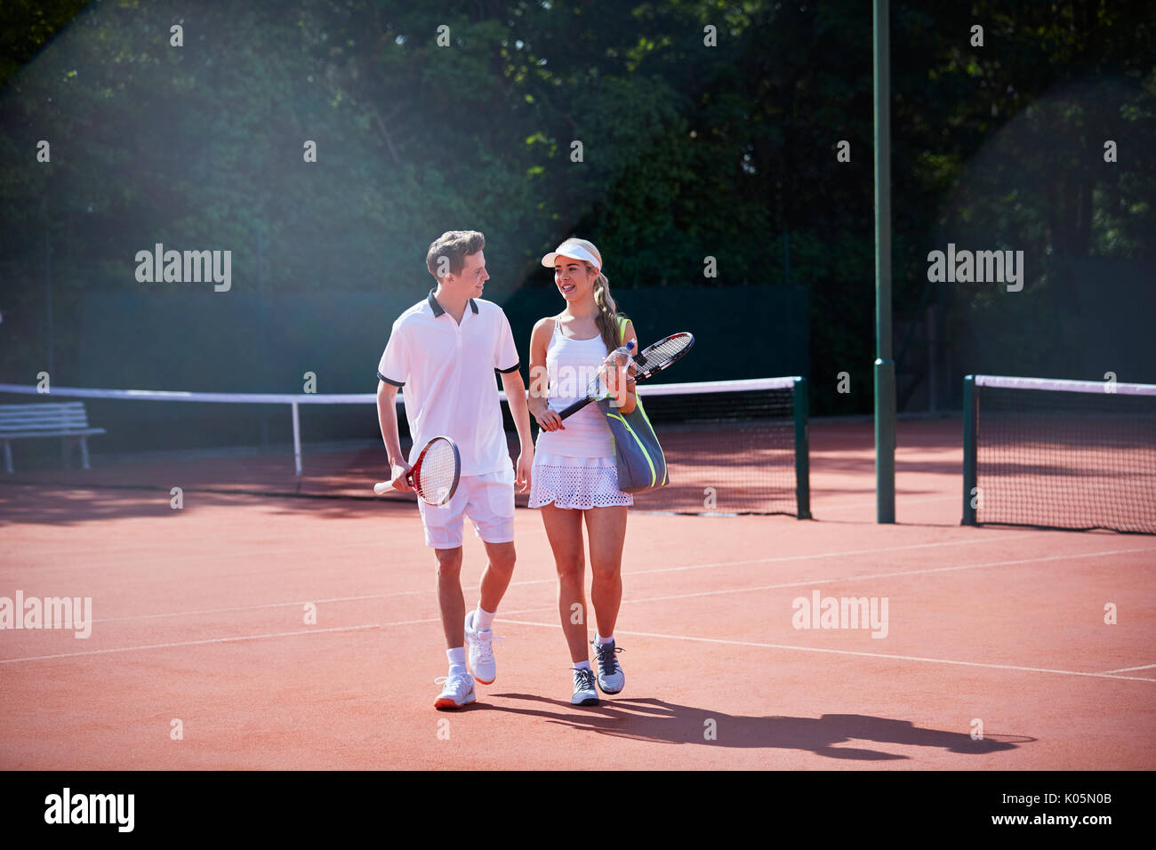 Tennis player couple walking, carrying tennis rackets on sunny clay tennis court Stock Photo