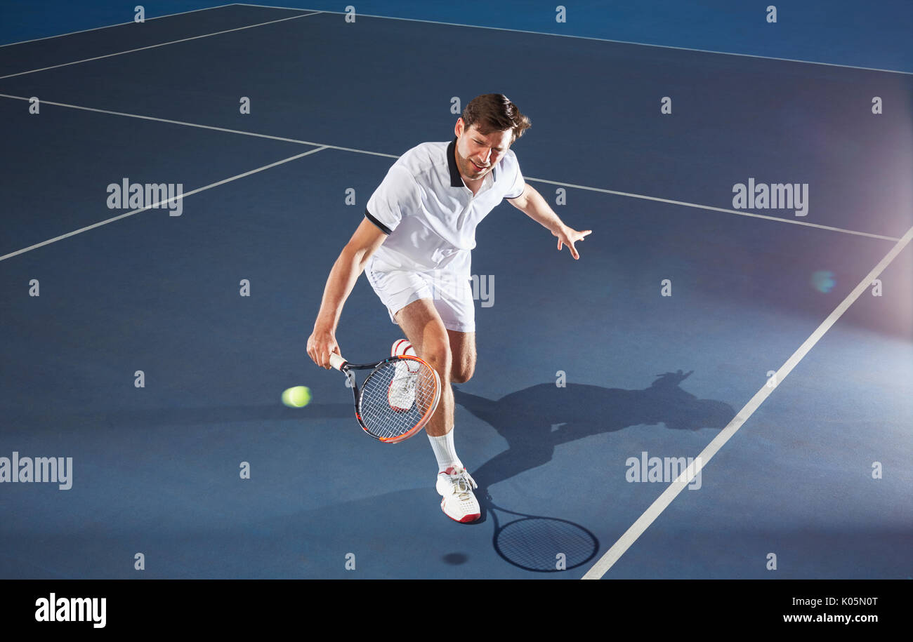Young male tennis player playing tennis, reaching with tennis racket on blue tennis court Stock Photo
