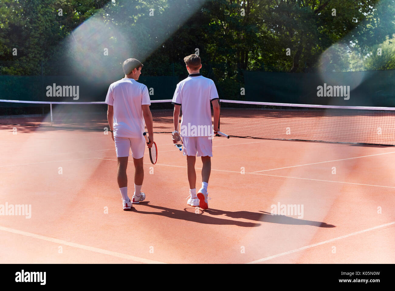 Young male tennis players walking with tennis rackets on sunny clay tennis court Stock Photo