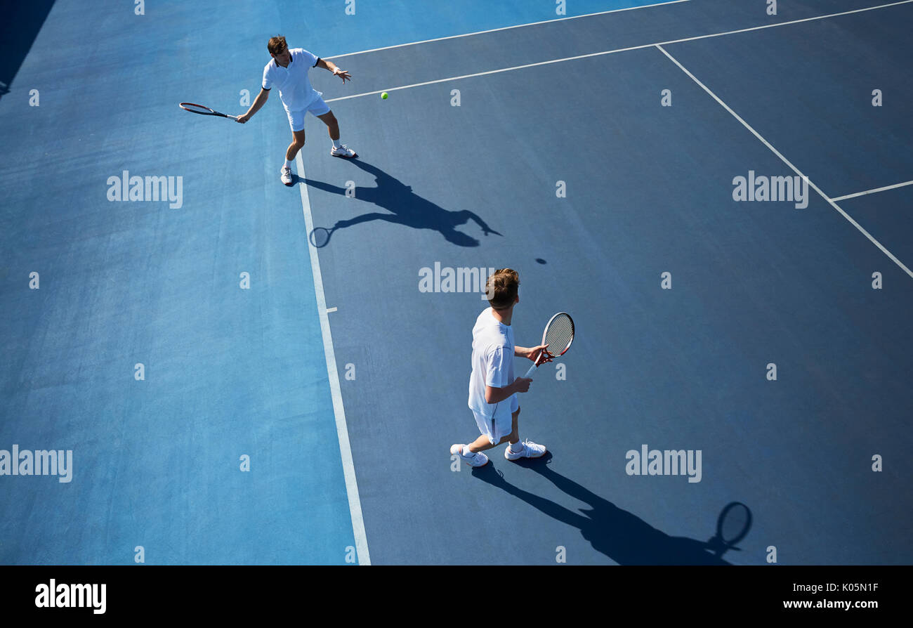 Young male doubles tennis players playing tennis on sunny blue tennis court Stock Photo