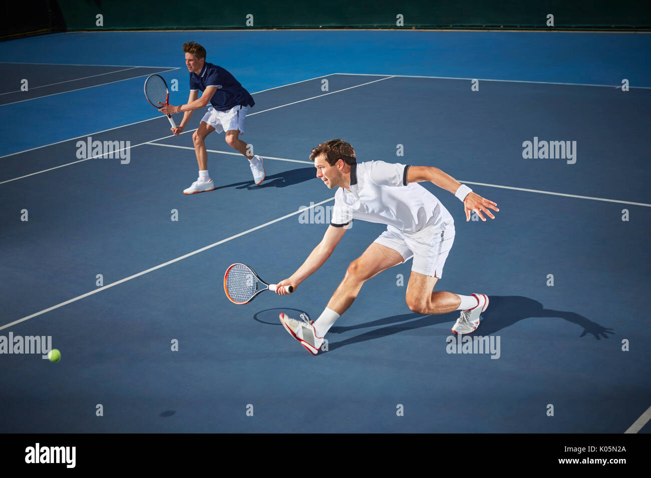 Young male tennis doubles players playing tennis, reaching with tennis racket on blue tennis court Stock Photo