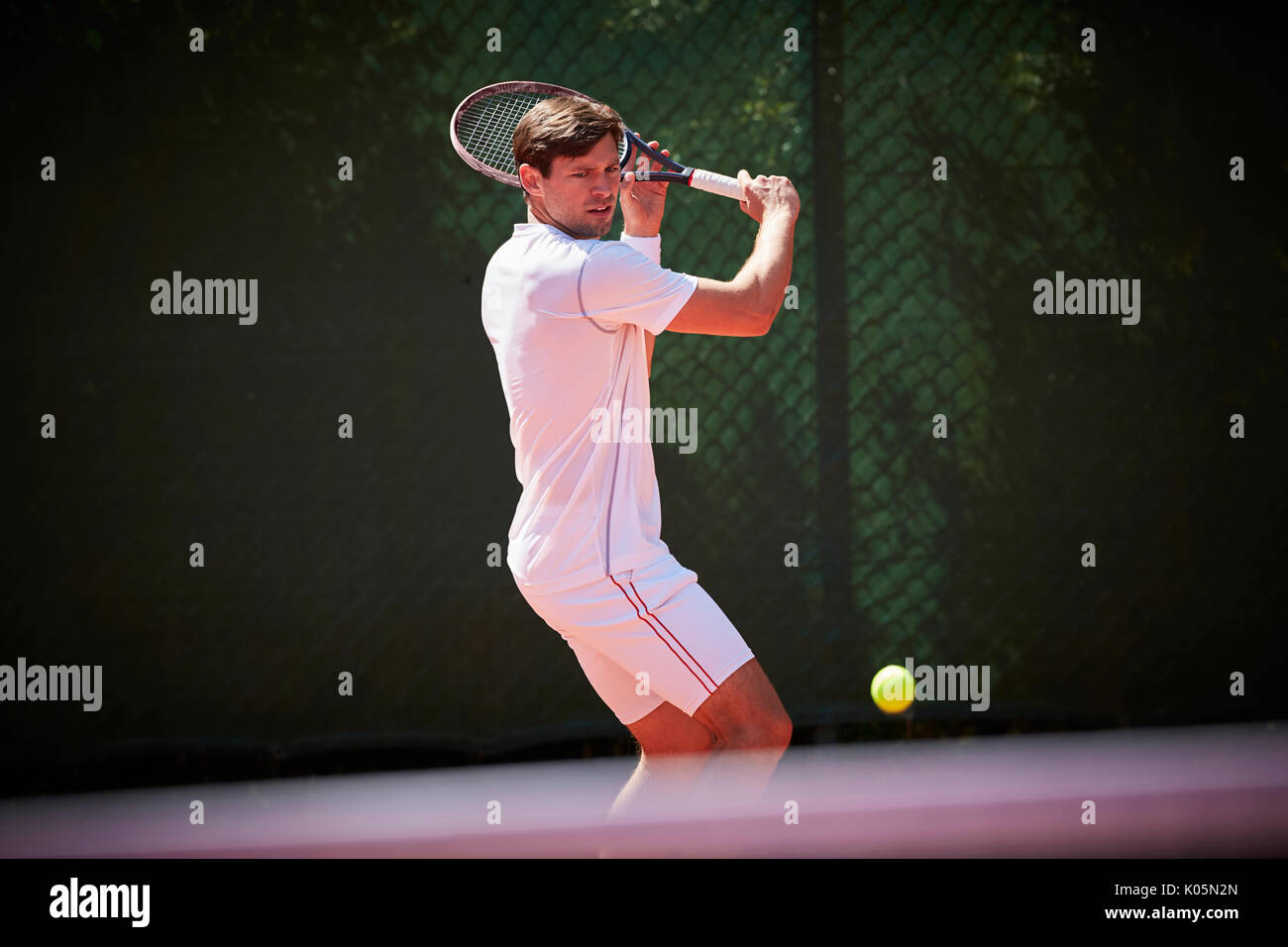 Young male tennis player playing tennis, swinging at tennis ball on sunny tennis court Stock Photo