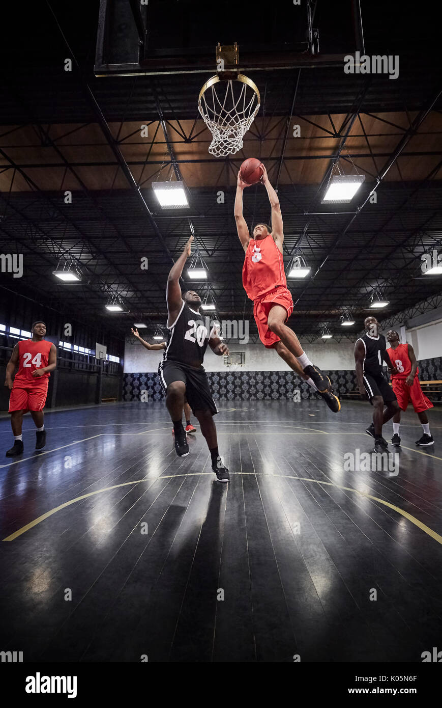 Young male basketball player jumping to slam dunk basketball in game on
